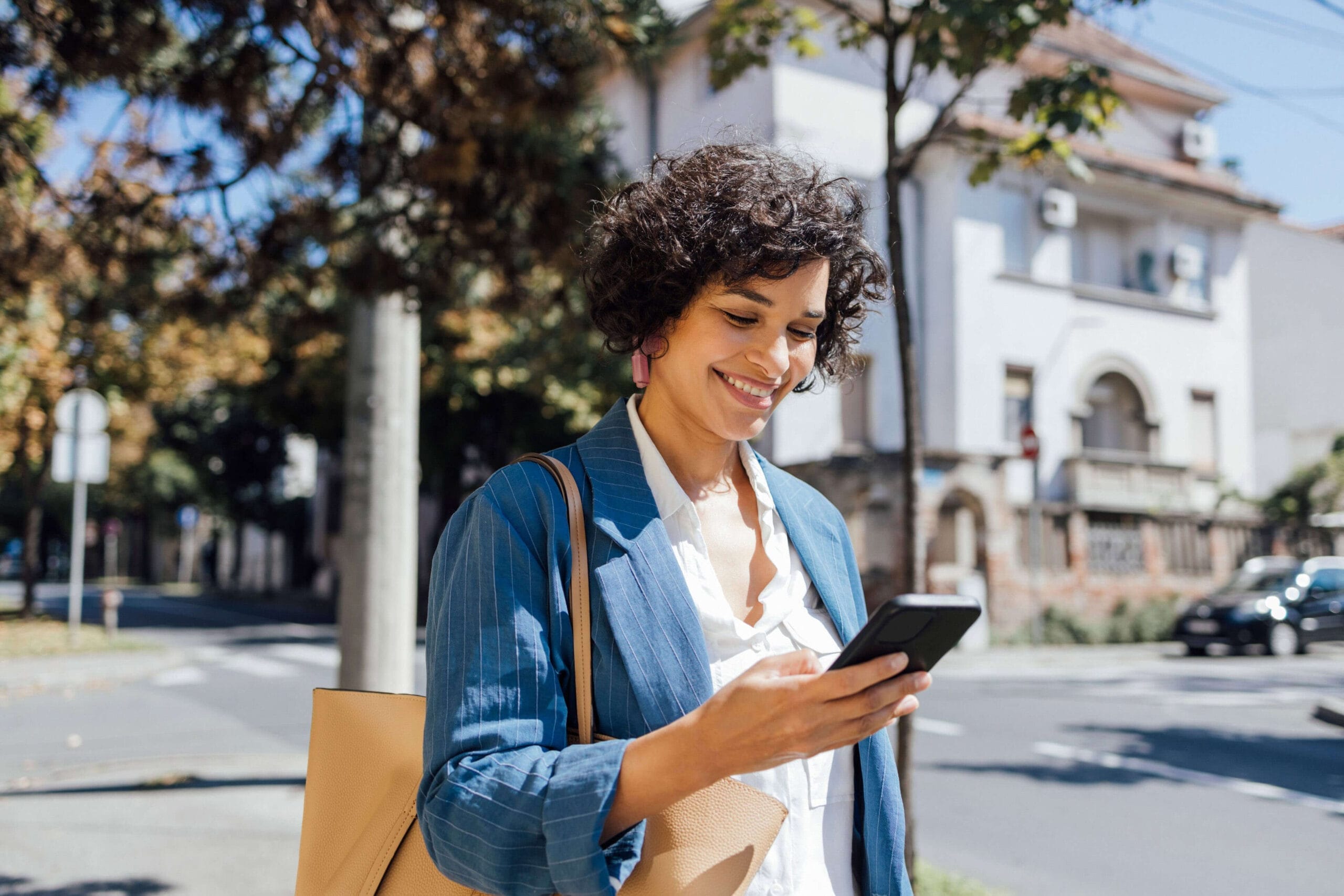 A woman is on the street, holding her phone, appearing focused and connected to her digital device.